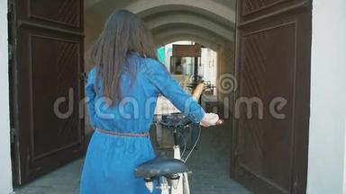 后景：一个黑发女孩骑着自行车走进老城的老门，慢影，稳重的镜头